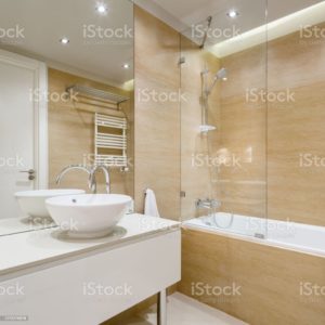 Elegant bathroom with beige tiles, stylish washbasin, big bathtub and shower and ceiling light